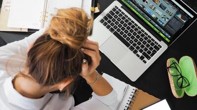 Vrouw zit voor haar laptop met haar handen in haar haar