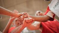 Sporters staan in een cirkel en leggen hun handen en vuisten op elkaar om samen te roepen